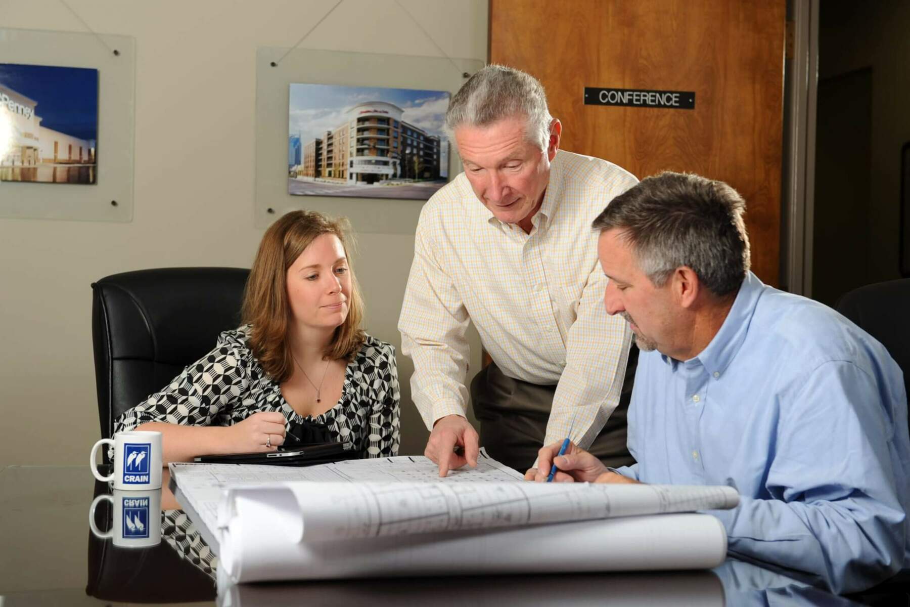The Crain Construction team reviewing construction plans leaning over a in a conference room table.