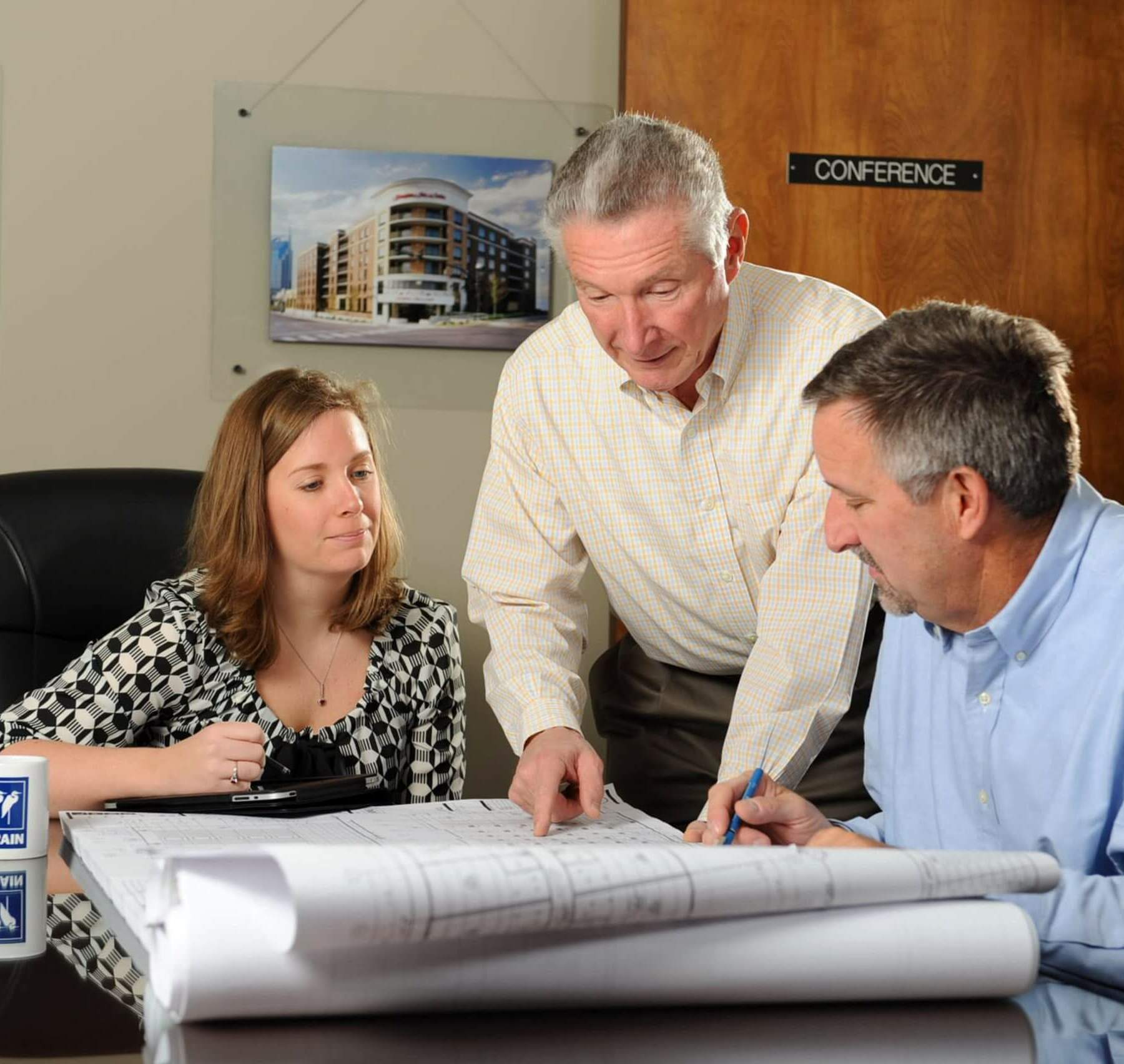 The Crain Construction team reviewing construction plans leaning over a in a conference room table.