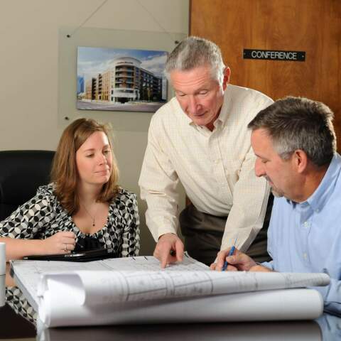 The Crain Construction team reviewing construction plans leaning over a in a conference room table.
