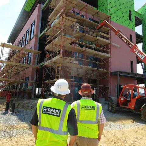 Two construction workers looking at a building that has been wrapped in weather-protecting materials