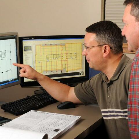 A contractor and an architect discussing a project while pointing at a computer.