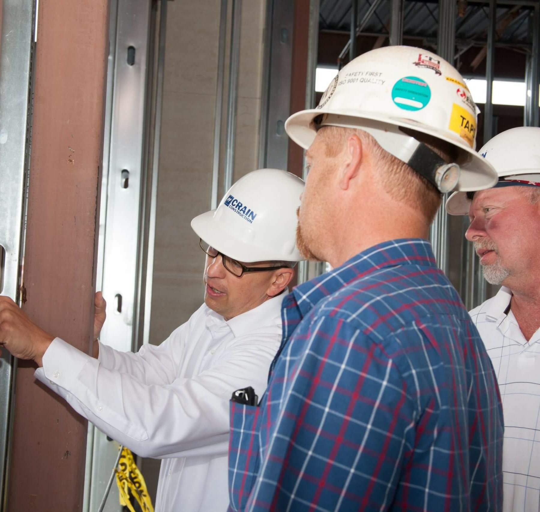 Three construction workers looking at the inside of a framed building with hard hats on.