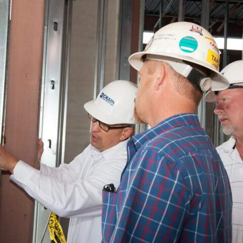 Three construction workers looking at the inside of a framed building with hard hats on.