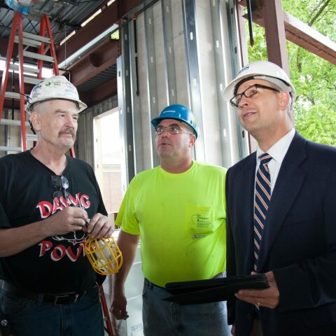 1 project manager with an iPad and 2 construction employees stand together in a construction site