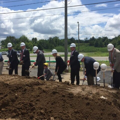 Crain employees breaking ground with shovels and hard hats at an unnamed job site on a sunny day