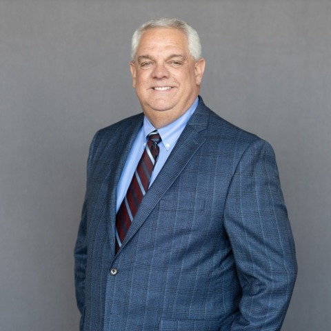 Portrait of Jim Pedigo wearing professional attire, with a friendly smile, in a well-lit indoor setting.