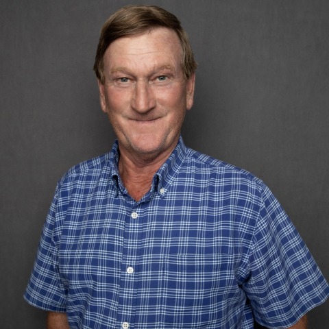 Portrait of JR Howell, a senior superintendent at Crain Construction, in professional attire, smiling and standing against a plain grey background.