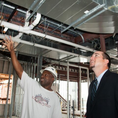 construction worker with hardhat showing project under construction to man in suit