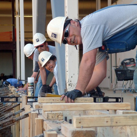 Smiling construction workers standing over beams.