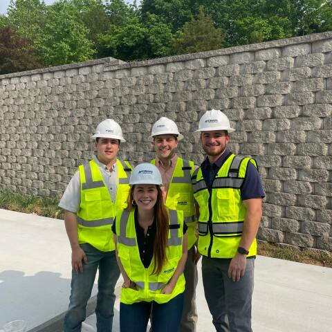 4 Crain Construction workers smiling in hard hats with neon vests on in front of a brick wall