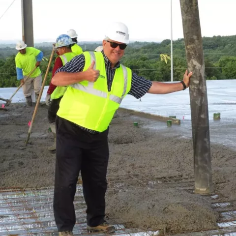 A man in a hard hat giving a thumbs up on a construction site.